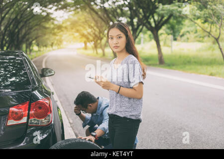 Asian woman using mobile phone while looking and Stressed man sitting after a car breakdown on street Stock Photo