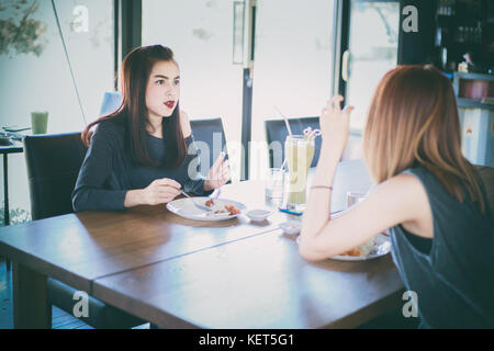 Two young female friends laugh and Having Lunch Together At Restaurant Stock Photo