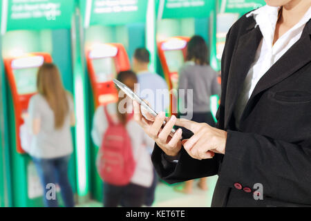Businessmen and women are using mobile and touch smart phone for Communication and checking on  People stand in line to withdraw money at ATM selectiv Stock Photo