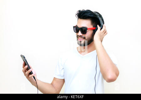Asian handsome man with a mustache, smiling and laughing and using smart phone to listen music with headphones ,Blurry and soft focus Stock Photo