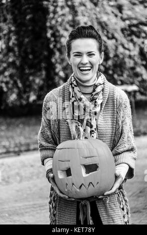 Trick or Treat. smiling modern woman on Halloween outdoors showing carved big pumpkin Stock Photo