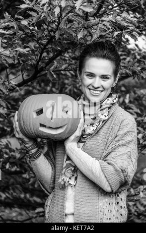 Trick or Treat. smiling modern woman on Halloween at the park showing pumpkin Jack O'Lantern Stock Photo