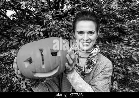 Trick or Treat. smiling modern woman on Halloween at the park showing carved pumpkin Stock Photo