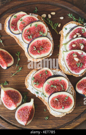 Bruschetta with fresh purple figs, ricotta cheese and honey on wooden cutting board garnished with fresh thyme and pine nuts. Healthy gourmet snack or Stock Photo