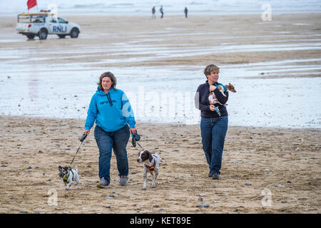 Dog walking - two women walking their small dogs on Fistral Beach Newquay. Stock Photo