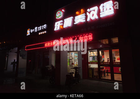 Hangzhou, China - December 3, 2014: Chinese night city street with bright advertisement neon lights on the wall of Fast Food restaurant Stock Photo