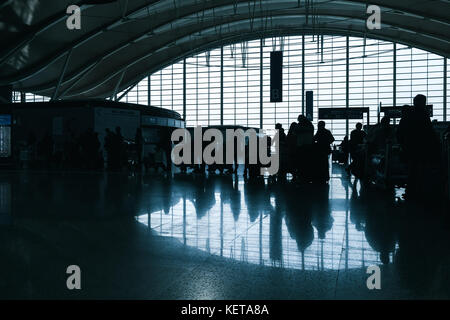 Shanghai, China - December 6, 2014: Passengers are in a waiting hall of Shanghai Pudong International Airport. Dark back lit photo with silhouettes Stock Photo