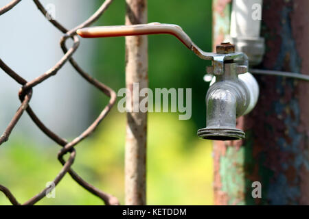 Close up of grunge brass faucet on green bokeh background. Water shortage and earth day concept. Stock Photo