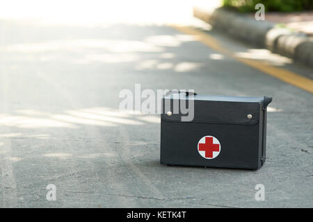 The vintage first aid kit box is made of black leather on the street floor of the park. The symbol is a red cross as a medical marker. Suitable for us Stock Photo