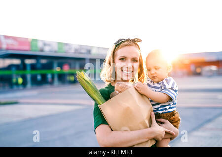 Young mother with baby boy in front of a supermarket. Stock Photo