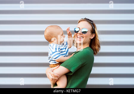 Young woman with a baby boy standing against the wall. Stock Photo