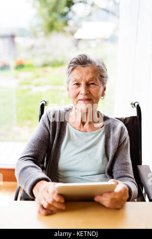 Senior woman in a wheelchair with tablet at home. Stock Photo