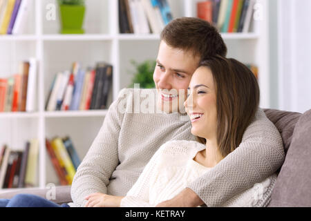 Portrait of a happy couple hugging looking away sitting on a couch at home Stock Photo