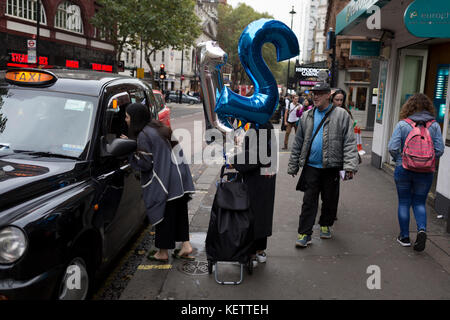 Young women hail a black cab while carrying 21st birthday balloons, on Charing Cross Road, on 19th October 2017, in London, England. Stock Photo