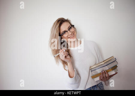 Beautiful girl happy, went to College, passed exams. Cute blonde with stack of books in hand Stock Photo