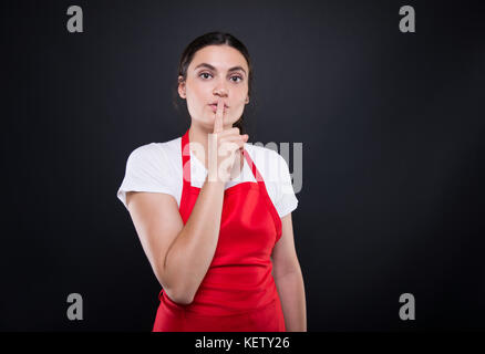 Beautiful seller with red apron doing silence gesture on dark background Stock Photo