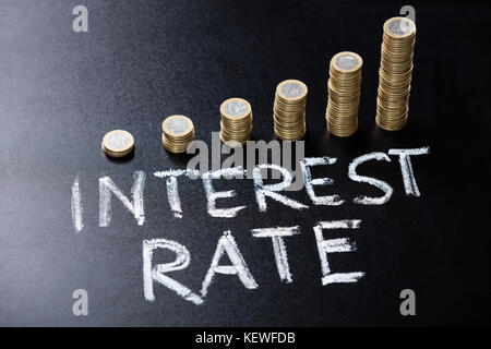 High Angle View Of Stacked Coin With Interest Rate Concept Written On Blackboard Stock Photo