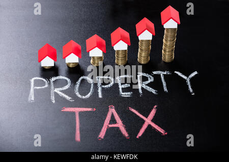 House Models On Stacked Coins Showing Property Tax Concept On Blackboard Stock Photo