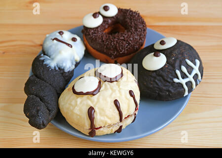 Plate of Assorted Halloween Monsters and Ghosts Shaped Doughnuts Served on Wooden Table Stock Photo