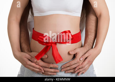 Midsection Of Man Embracing Pregnant Woman's Belly Tied With Red Ribbon Stock Photo