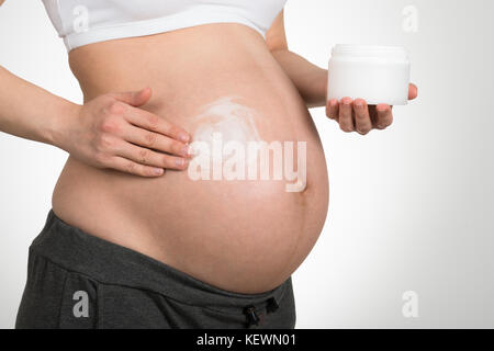 Expecting Woman Applying Cream On Her Belly Over Grey Background Stock Photo