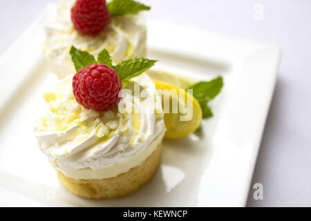 Two small Lemon Cakes with whipped cream topping garnished with a raspberry and mint leaves. Stock Photo