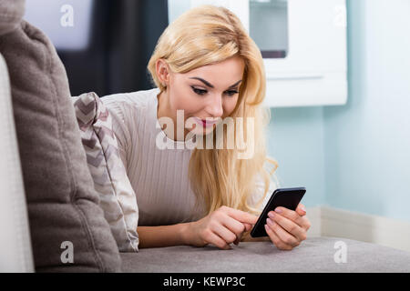 Close-up Of Young Woman Lying On Sofa Using Mobile Phone At Home Stock Photo