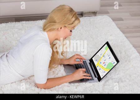 A Young Woman Lying On Carpet Using GPS Navigation Map On Laptop Computer At Home Stock Photo