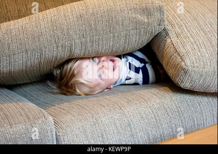 Little boy hiding under sofa cushions Stock Photo