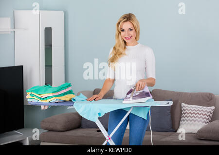 Young Smiling Woman Ironing Clothes On Ironing Board At Home Stock Photo