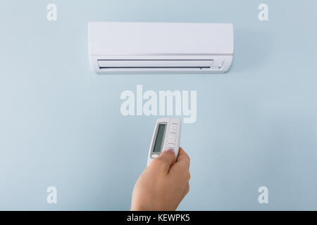 Close-up Of Young Woman Hand Operating Air Conditioner With Remote Control Stock Photo