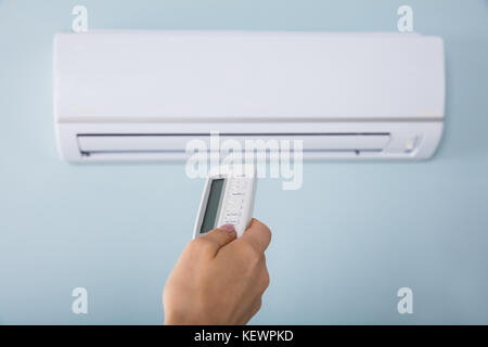 Close-up Of Young Woman Hand Operating Air Conditioner With Remote Control Stock Photo
