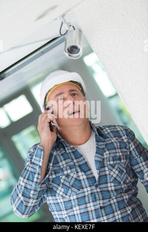 Contractor looking at security camera and talking on telephone Stock Photo