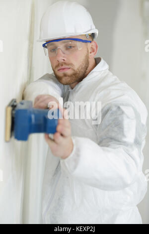 young builder in hardhat sanding wall indoors Stock Photo