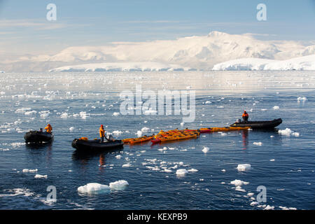 Members of an expedition cruise to Antarctica in a Zodiak with sea kayaks in Fournier Bay in the Gerlache Strait on the Antarctic peninsula. The Antarctic peninsula is one of the most rapidly warming areas on the planet. Stock Photo