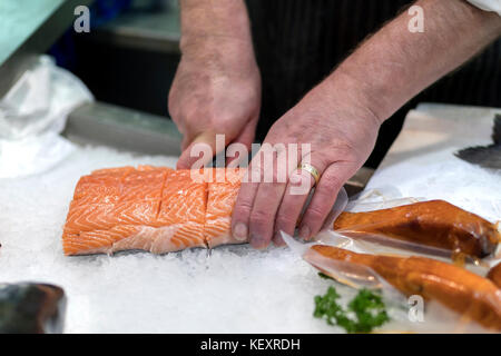 British fish monger slicing, filleting or cutting fresh slamon on ice on a market staff in Yorkshire, England Stock Photo