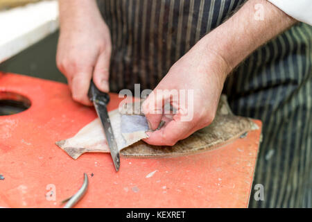 British fish monger fillets a dover sole and pulls it’s skin away on a market stall in Yorkshire, England, UK Stock Photo
