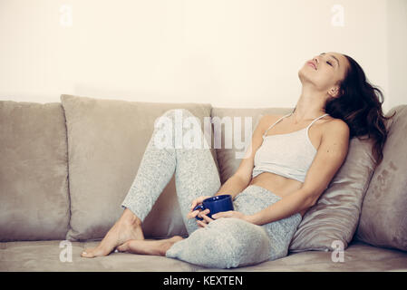 Young pretty asian woman sitting on the couch relaxed smiling face expression blue mug in the hands Stock Photo