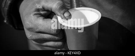 Dirty Beggar Hand Holding Plastic Cup. Poor Man Begging for Money on the Street Close Up. Stock Photo