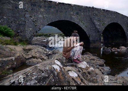 17 year old girl writes in her journal at old stone bridge over River Slichagan  Isle of Skye, Scot Stock Photo