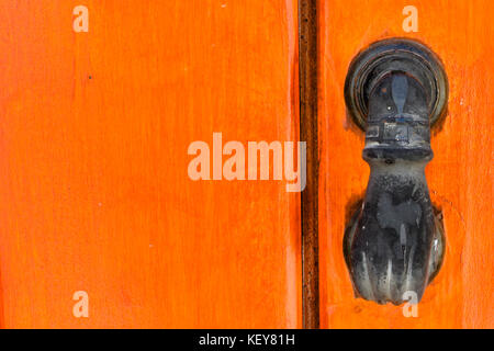 Old door knocker shaped as a hand on an orange door in Crete, Greece Stock Photo