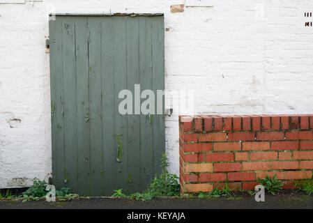 Old faded green wooden door with flaky paint in white brick wall Stock Photo