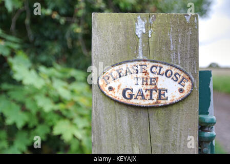 Weathered old Please Close The Gate sign on wooden post with path in the background Stock Photo