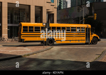 A yellow old fashioned school bus driving via streets of downtown in Toronto, Canada Stock Photo