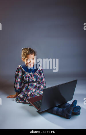 little girl looking at laptop rejoices over gray background Stock Photo