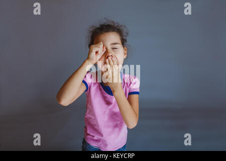 girl yawns t hand over his eyes on a gray background Stock Photo