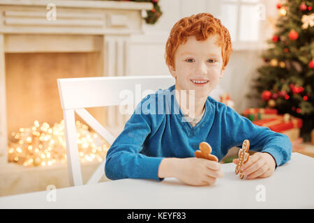 Charming ginger kid smiling while playing with gingerbread men Stock Photo