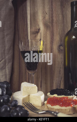 A glass of red wine, Brie cheese, grapes and caviar Stock Photo