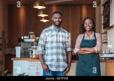 Two smiling African entrepreneurs standing at their cafe counter Stock Photo