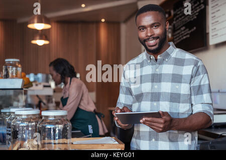 Smiling African entrepreneur working at the counter of his cafe Stock Photo